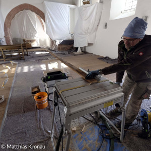 Schreinermeister Bernhard Popp bei der Arbeit. Man erkennt den neuen Holzfußboden unter den (noch fehlenden) Bänken mit den Zuleitungen für die elektrische Sitzbankheizung.